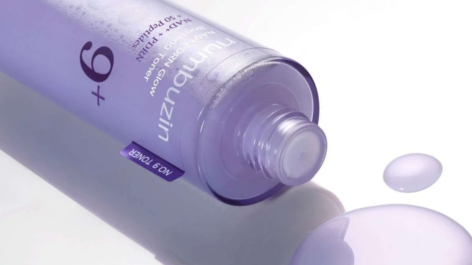 En vit flaska Anua Heartleaf 77% Soothing Toner ligger på en vågig grön yta, täckt av vattendroppar.