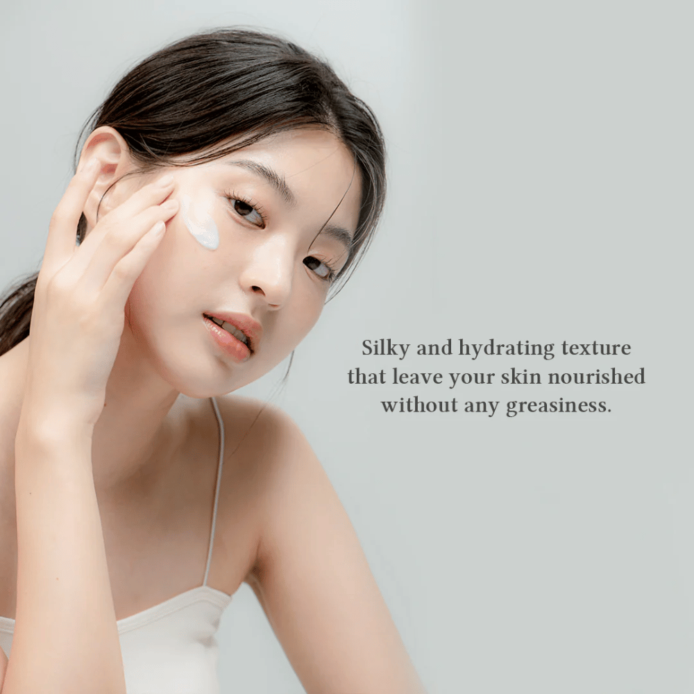 L'immagine mostra una donna che applica una crema per il viso. Il testo sull'immagine descrive il prodotto come setoso e idratante, sottolineando che nutre la pelle senza lasciare una sensazione oleosa. Ciò suggerisce che la crema ha una consistenza leggera e piacevole che viene ben assorbita dalla pelle.
