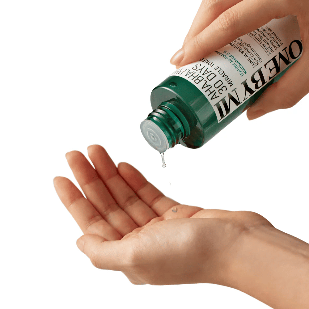 Una mano tiene una bottiglia verde con il testo "AHA, BHA, PHA 30 Days Miracle Toner" e versa un liquido trasparente nel palmo dell'altra mano, pronto per l'uso.