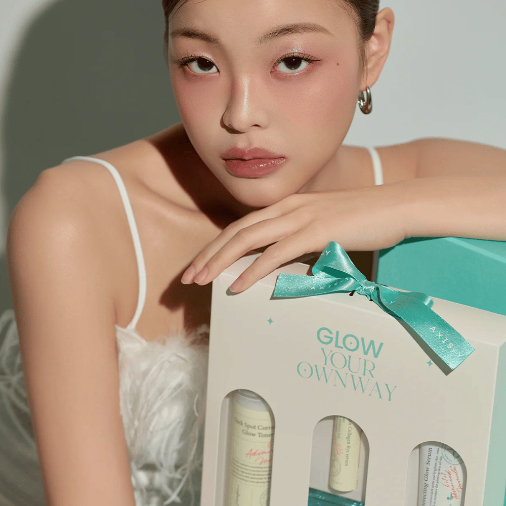 Modella con trucco elegante tiene in mano la confezione regalo "Glow Your Own Way" di AXIS-Y – un kit di cura della pelle dal design elegante perfetto come regalo per te stesso o per qualcuno che ami.