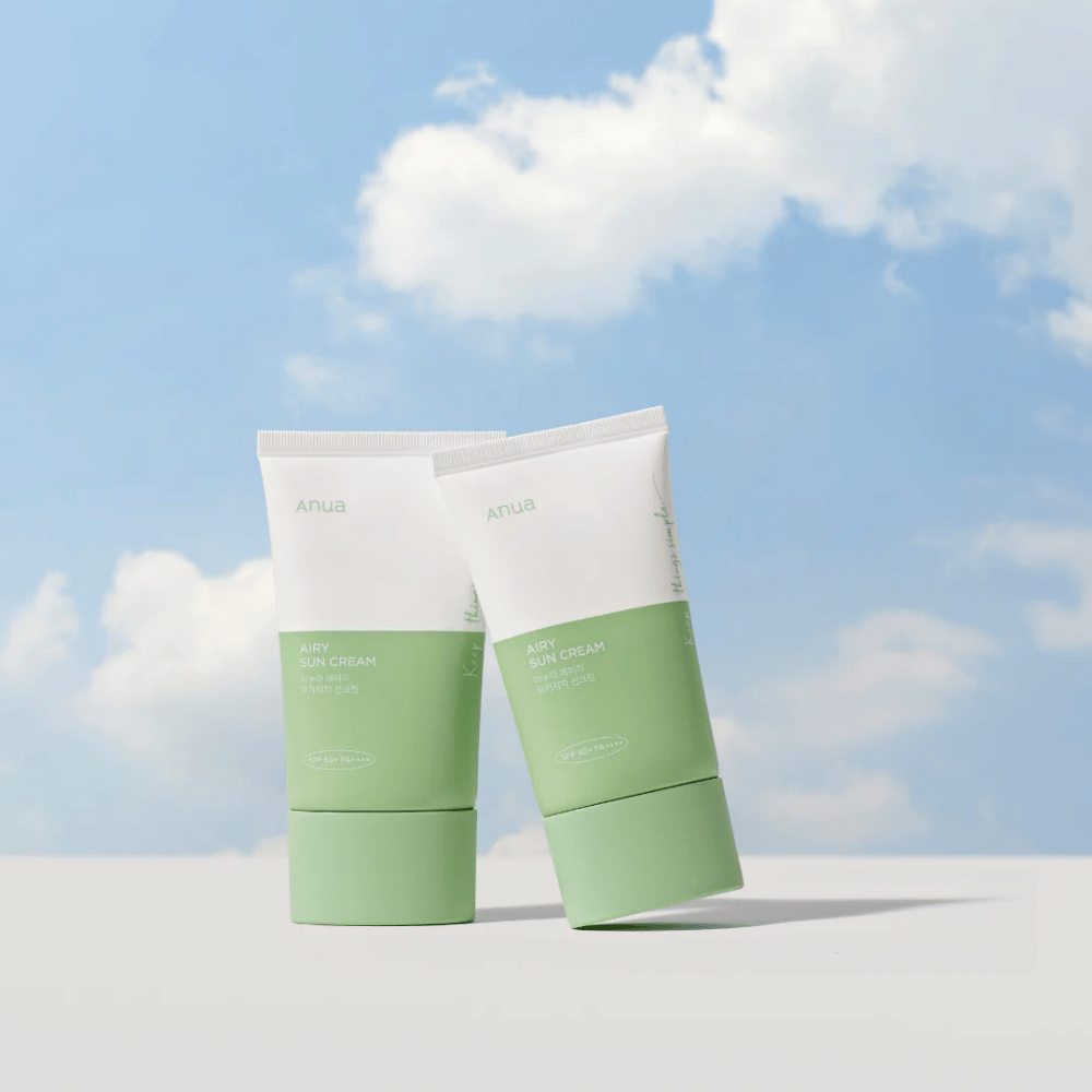 Due tubi di Anua Airy Sun Cream contro un cielo con nuvole bianche.