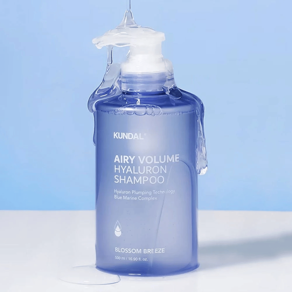 KUNDAL Airy Volume Hyaluron Shampoo Blossom Breeze in flacone pompa blu, con acido ialuronico e Blue Marine Complex, fotografato con acqua corrente.