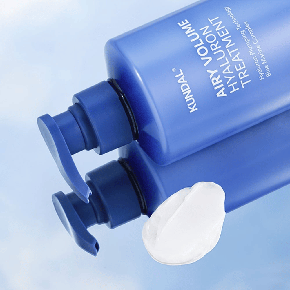 KUNDAL Airy Volume Hyaluron Treatment in bottiglia a pompa blu sdraiata, con prodotto cremoso bianco visibile accanto.