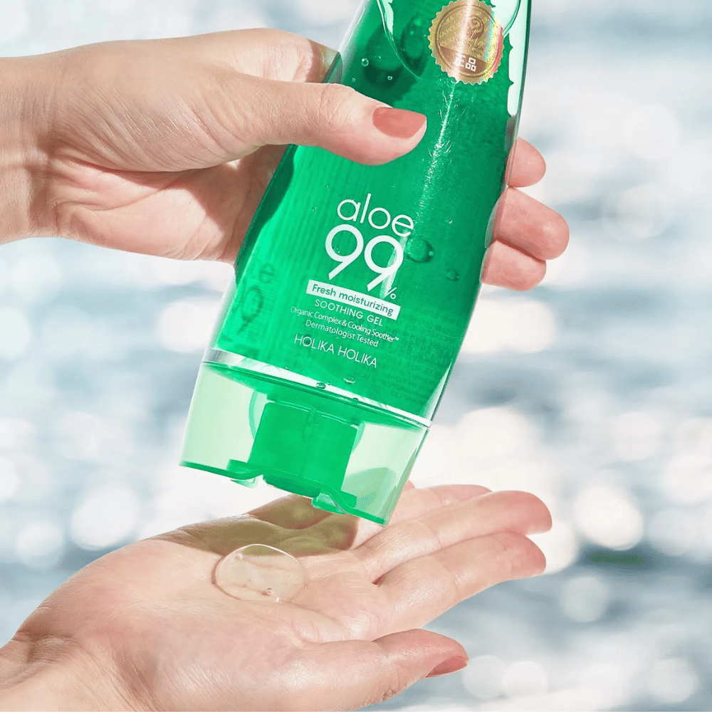 Una mano tiene un tubetto verde con Holika Holika Aloe 99% Soothing Gel, mentre un'altra mano raccoglie una goccia di gel che viene erogata. Lo sfondo è sfocato e mostra un motivo acquatico e scintillante.