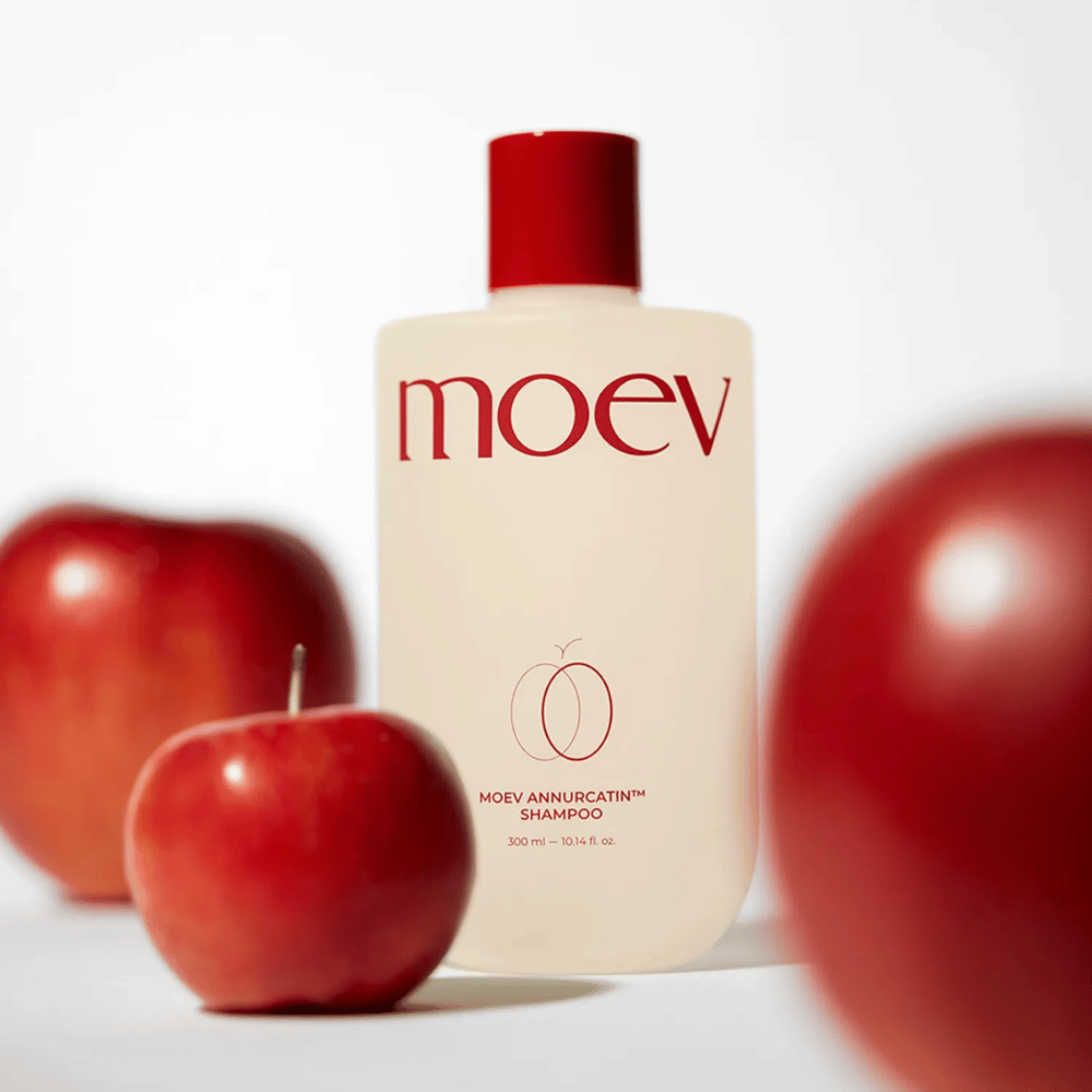 MOEV Annurcatin Shampoo posizionato tra mele rosse – ispirato dagli antiossidanti della mela Annurca che donano capelli più forti, sani e lucenti.