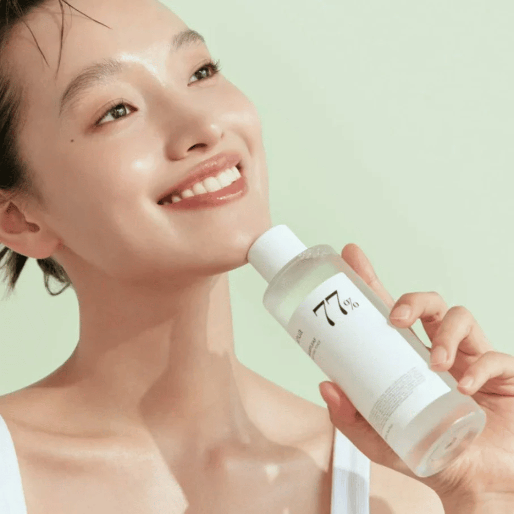 Una donna calma la sua pelle sensibile con una bottiglia Heartleaf 77% Soothing Toner da Anua, contenente estratto di foglie di camaleonte.
