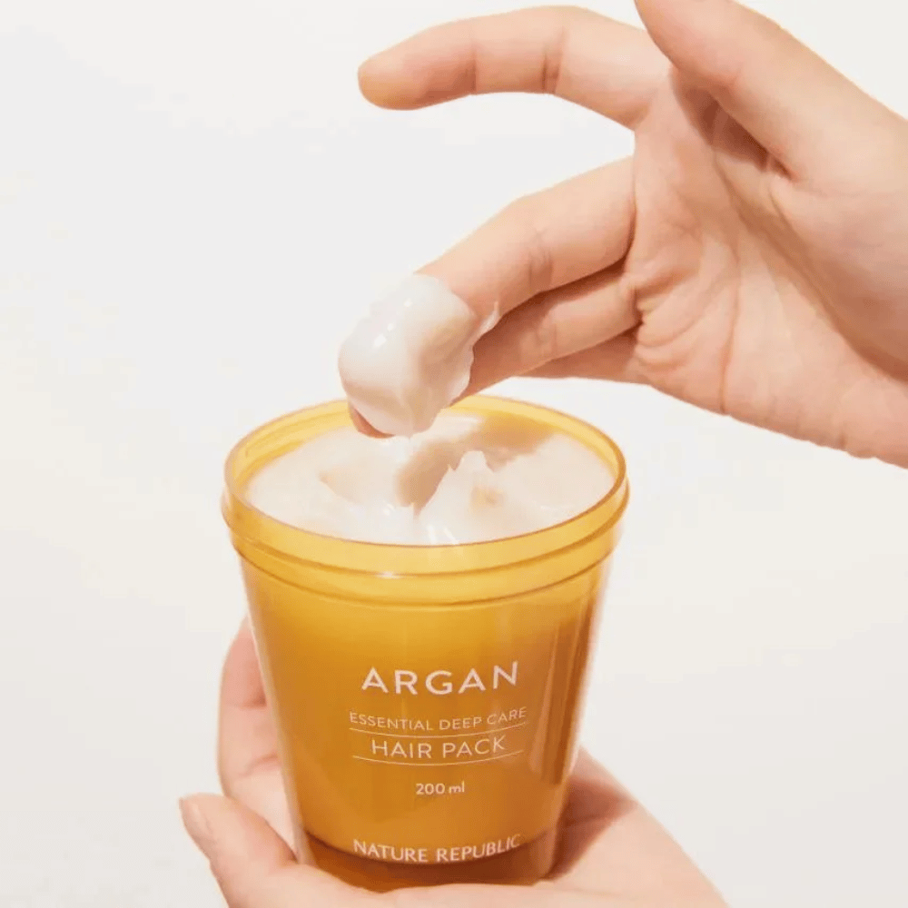 La mano prende la formula cremosa da Nature Republic Argan Essential Moisture Repairing Hair Mask – nutrizione intensa per capelli secchi.