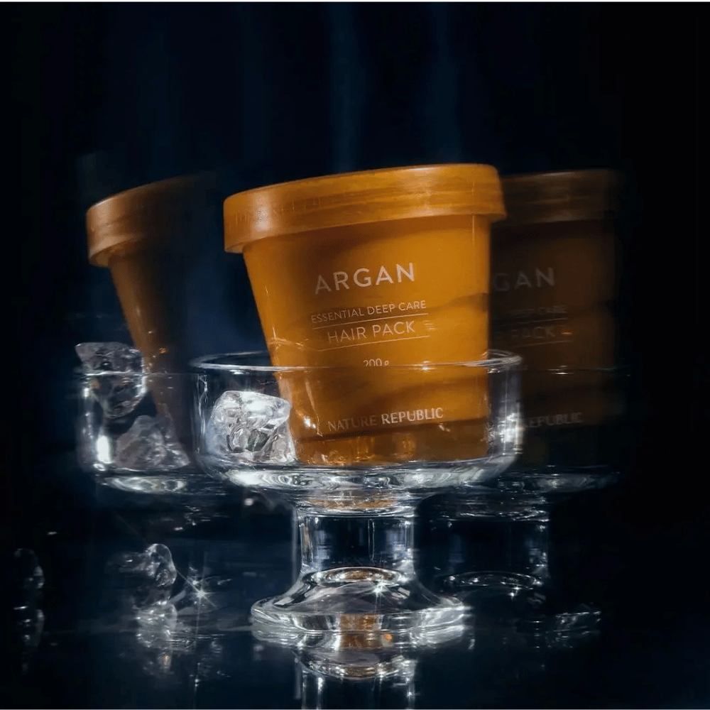Nature Republic Argan Essential Moisture Repairing Hair Mask posizionata su piatto di vetro con cubetti di ghiaccio – maschera per capelli lussuosa e curativa.