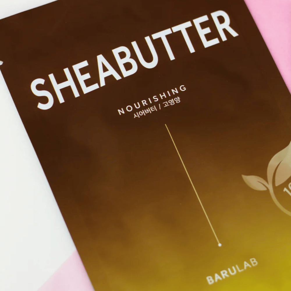 Un primo piano di una confezione di maschera "SHEABUTTER Nourishing" BARULAB. Il prodotto è etichettato come "100% Vegan Product" e ha un gradiente di colore dal marrone scuro al marrone chiaro.