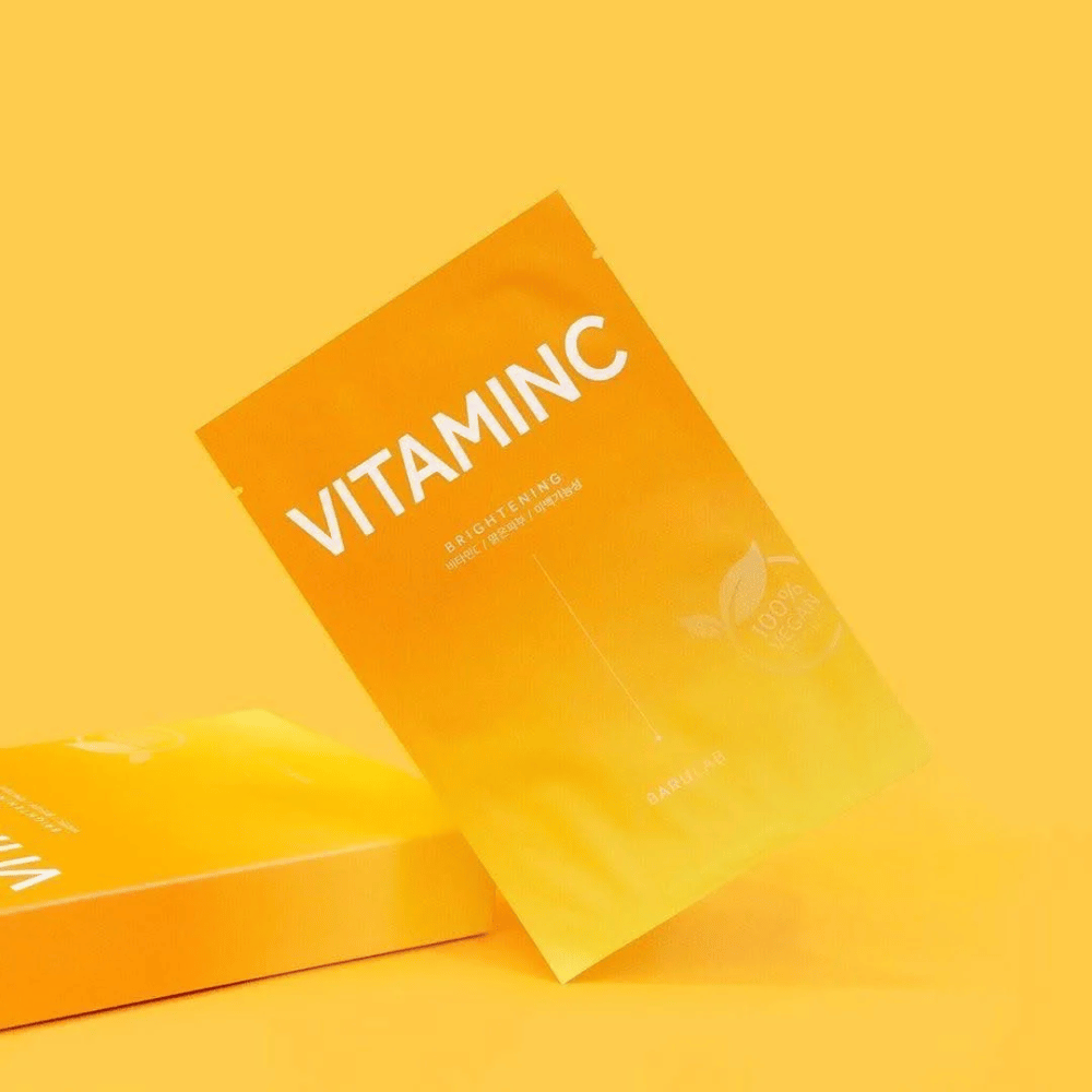 Un mucchio di confezioni di BARULAB maschere "VITAMINC Brightening", tutte etichettate come "100% Vegan Product". Le confezioni hanno una tonalità di colore in diverse sfumature di arancione e giallo, posizionate su uno sfondo giallo uniforme.