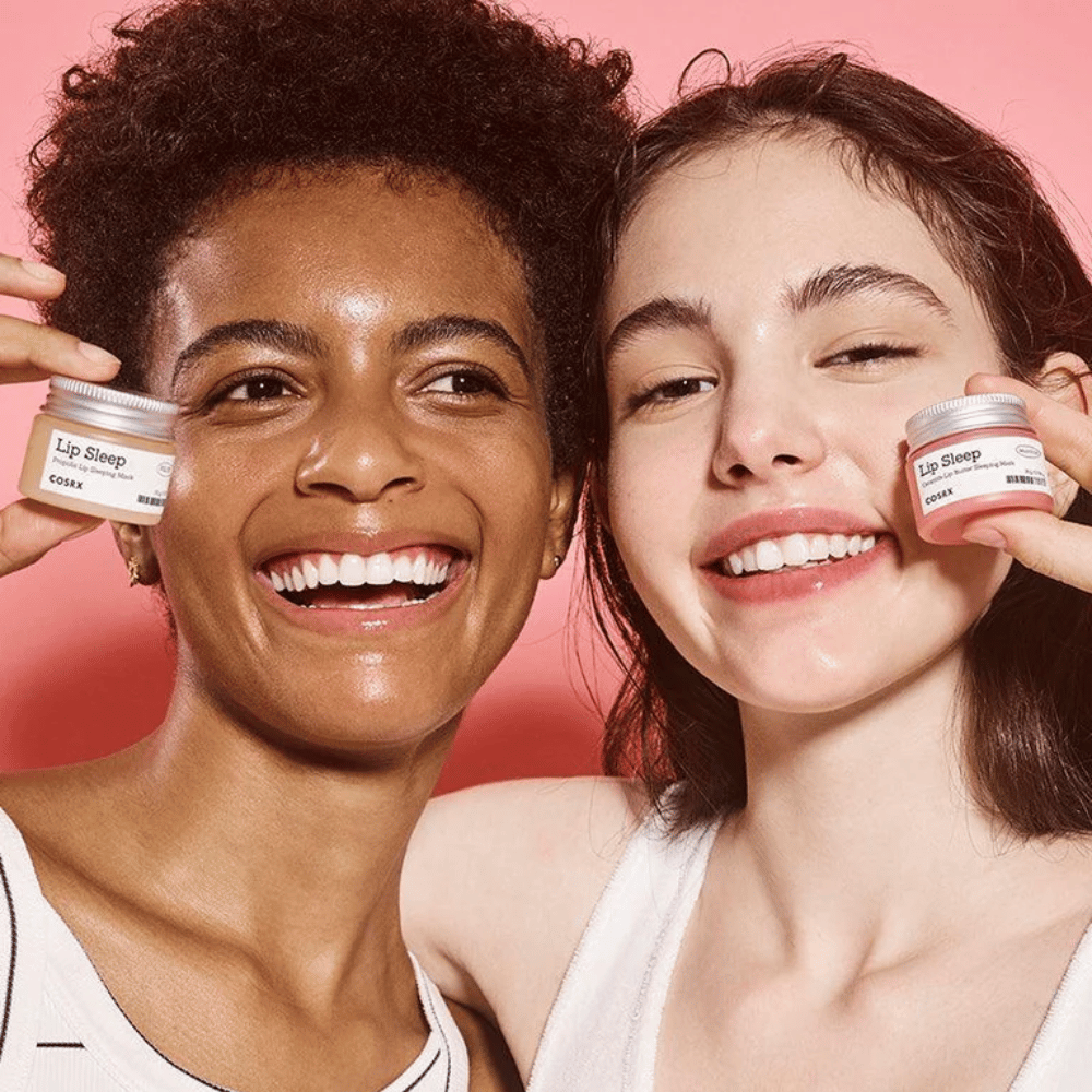 Due persone sorridono e tengono in mano barattoli di COSRX Lip Sleep. L'immagine trasmette labbra morbide e idratate e l'effetto naturale di luminosità del prodotto.
