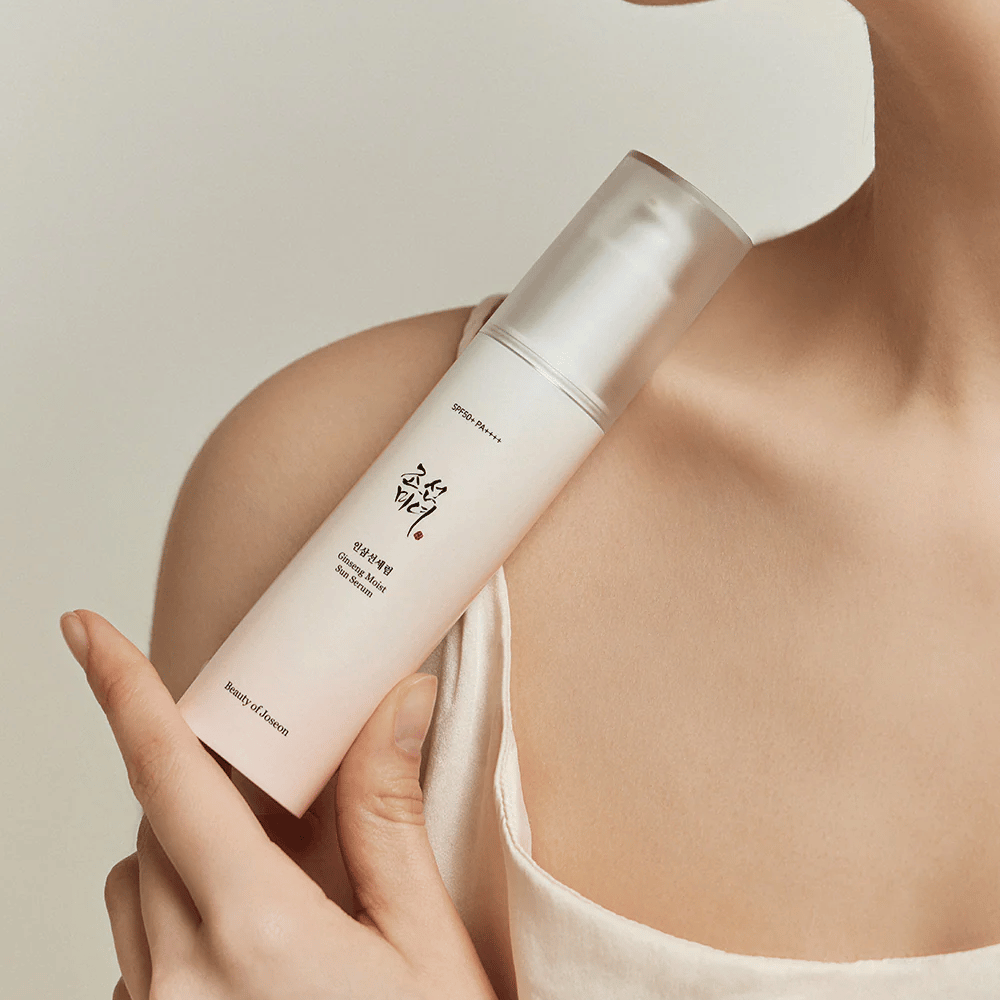 Una donna che tiene in mano una bottiglia di Beauty of Joseon's Ginseng Moist Sun Serum SPF 50+ PA++++, che offre protezione 50+ PA++++ e benefici per la cura della pelle.