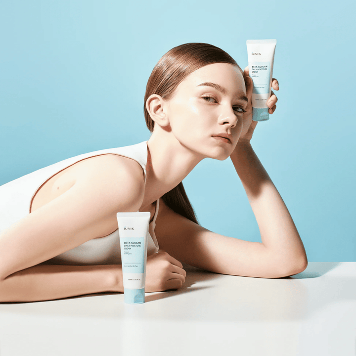 Immagine lifestyle in cui una modella posa con iUNIK Beta-Glucan Daily Moisture Cream su uno sfondo azzurro chiaro. L’immagine trasmette una sensazione pulita, fresca e idratante, mentre il prodotto viene esposto chiaramente.
