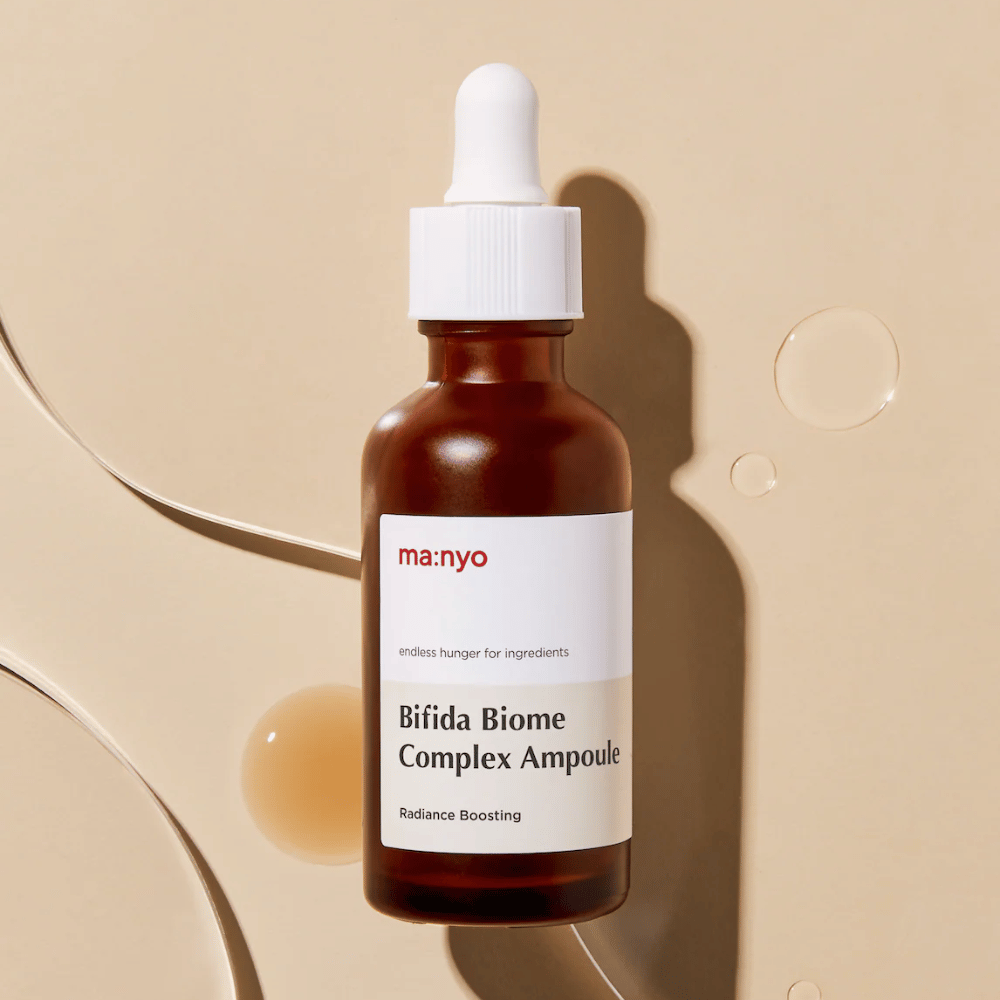 Elegante immagine del prodotto di ma:nyo Bifida Biome Complex Ampoule con focus sul design del flacone e gocce di siero sullo sfondo.