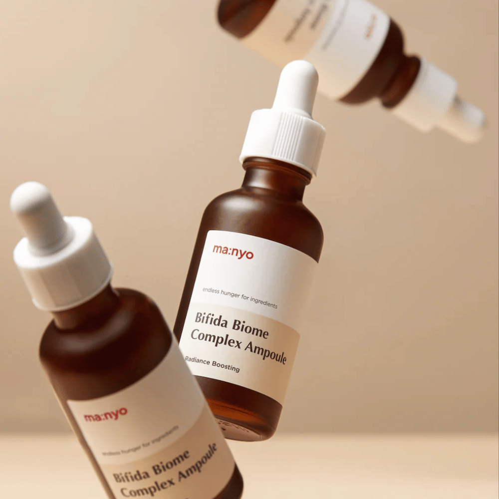 Immagine del prodotto con più flaconi sospesi di ma:nyo Bifida Biome Complex Ampoule su sfondo beige che conferisce una sensazione moderna e minimalista.