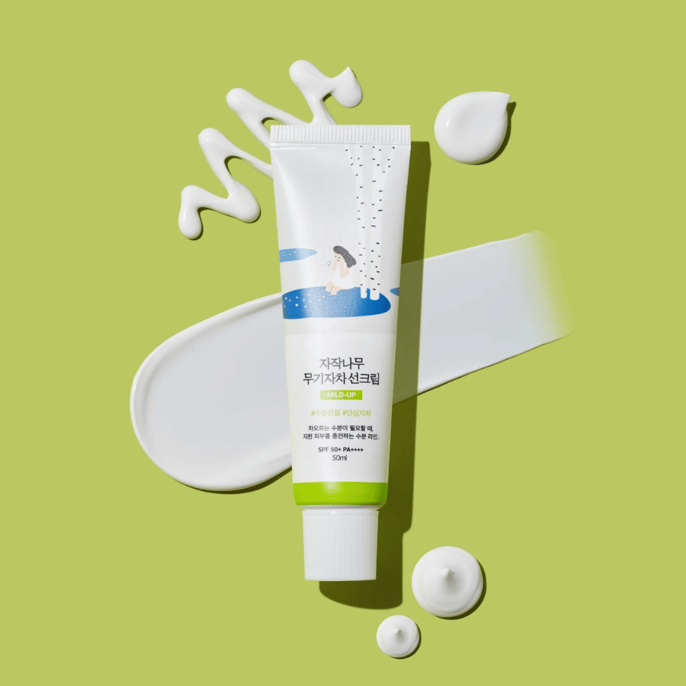 Birch Juice Moisturizing Mild Up Sunscreen – tubo bianco con base verde su sfondo verde, circondato da crema solare spalmata e gocce, SPF 50+ PA++++, 50 ml.