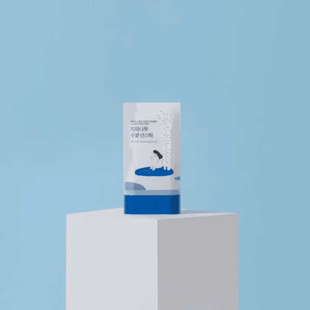 ROUND LAB Birch Juice Moisturizing Sun Stick SPF50+ si trova su un piedistallo su sfondo blu – protezione solare idratante in formato stick