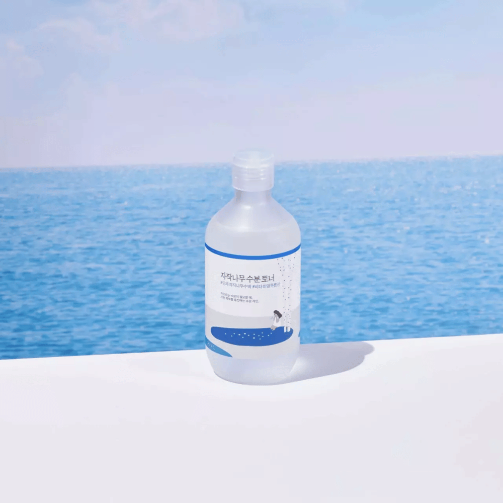 Flacone di ROUND LAB Birch Juice Moisturizing Toner su una superficie bianca con mare e cielo azzurro sullo sfondo