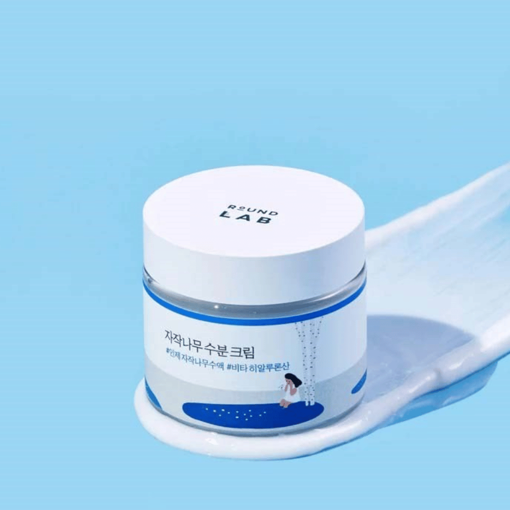 Round Lab Birch Juice Moisturizing Cream in barattolo blu con coperchio bianco, posizionato in uno strato di crema su sfondo blu.