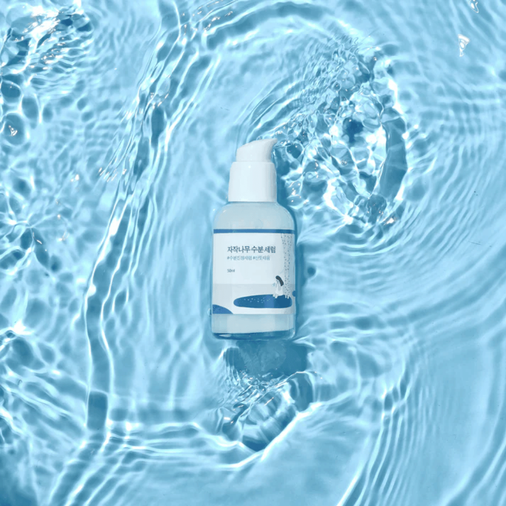 Round Lab Birch Juice Moisturizing Serum in flacone con pompa che galleggia su acqua blu con riflessi di luce solare.