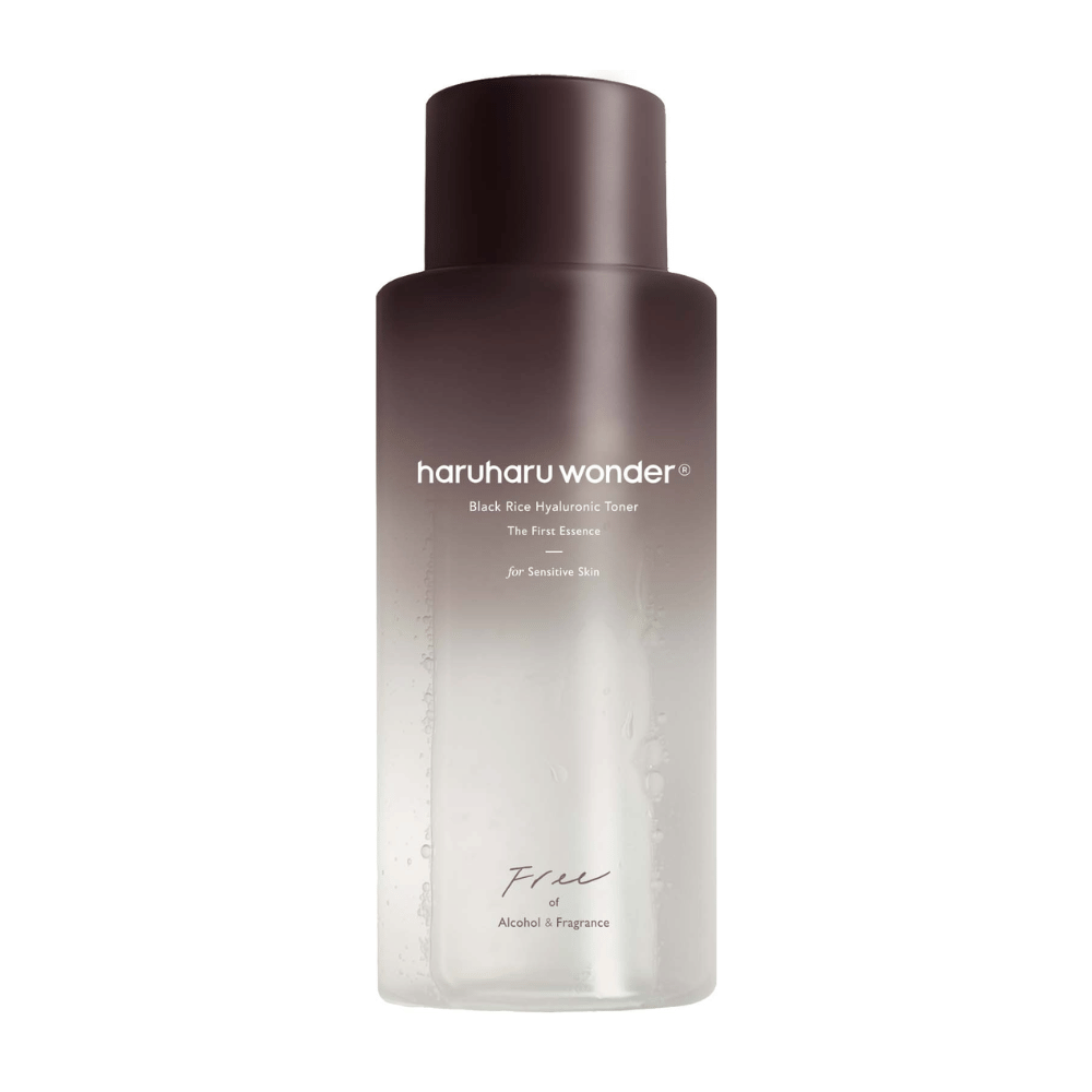 Una bottiglia di haruharu wonder Black Rice Hyaluronic Tonico viso The First Essence, con una gradazione dal marrone scuro al trasparente e il testo "Free of Alcohol & Fragrance", su sfondo bianco.