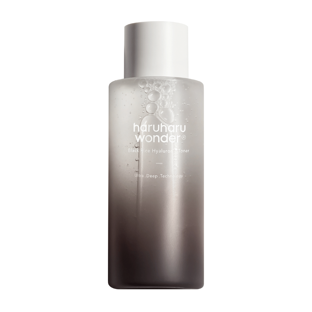 Una bottiglia di haruharu wonder Black Rice Hyaluronic Tonico viso con una gradazione di colore dal grigio al bianco e gocce d'acqua sulla superficie, su uno sfondo bianco.