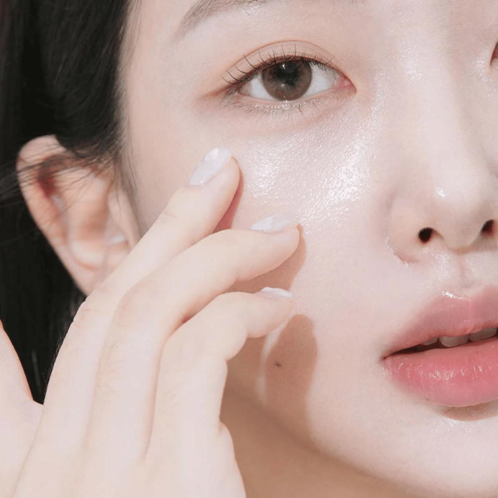 Primo piano di una donna che applica crema contorno occhi sotto l'occhio con la punta delle dita. La pelle appare idratata, lucente e curata con una luminosità naturale.