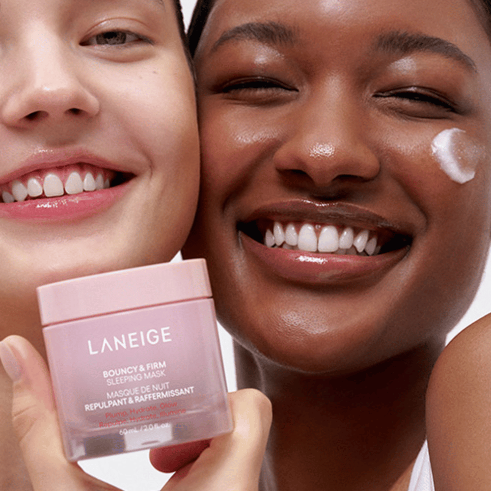Due persone sorridono e tengono in mano Laneige Bouncy & Firm Sleeping Mask. Una ha applicato la maschera sulla guancia, e il prodotto è chiaramente visibile nelle loro mani. La maschera è in un barattolo rosa e viene commercializzata come "Plump, Hydrate, Glow."