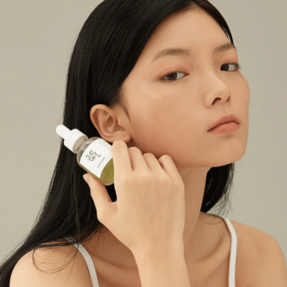 Modello tiene Beauty of Joseon Calming Serum sulla guancia – tè verde e pantenolo che rafforzano la barriera cutanea.