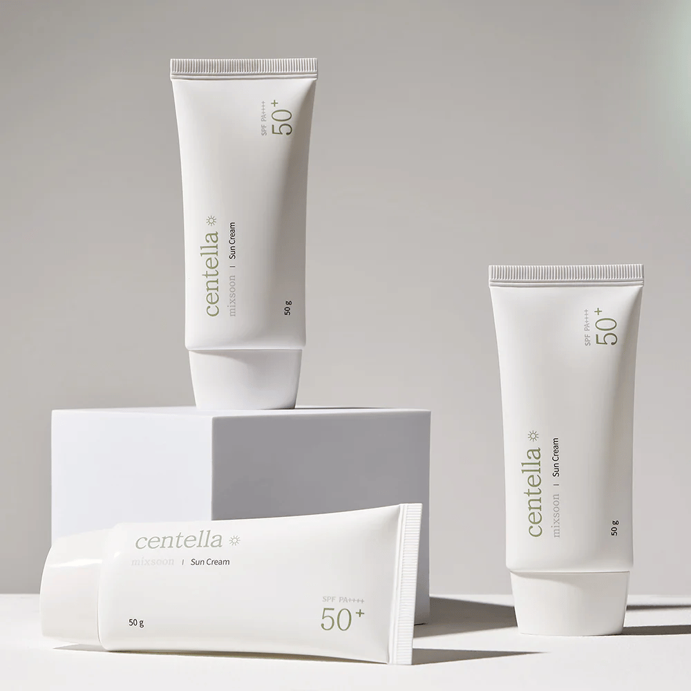 Tre confezioni di Centella Sun Cream SPF 50+ PA++++ disposte esteticamente su piedistalli bianchi. Due tubi sono in piedi e uno è sdraiato, tutti con un design bianco e minimalista e dettagli di testo verdi.