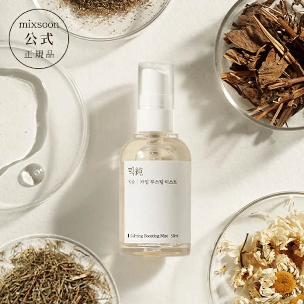 Un flacone spray trasparente con l'etichetta 'Calming Boosting Mist' di Mixsoon, circondato da erbe e fiori secchi in ciotole bianche su uno sfondo beige, che mette in risalto gli ingredienti naturali dei prodotti.