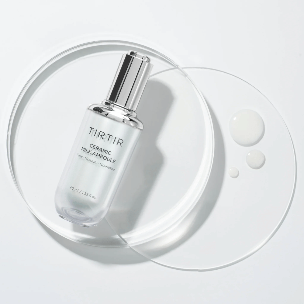Una bottiglia trasparente TIRTIR Ceramic Milk Ampoule su una lastra di vetro con gocce, su uno sfondo bianco, mette in risalto lucentezza, idratazione e nutrimento.