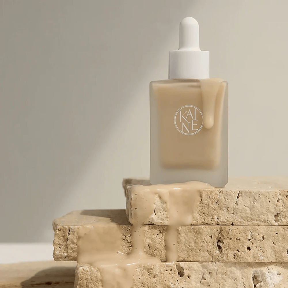 KANE Chaga Collagen Charging Serum in una bottiglia di vetro smerigliato con pipetta. La consistenza cremosa scorre su pietre naturali in una luce morbida e minimalista.