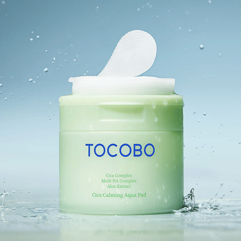 Barattolo aperto con TOCOBO Cica Calming Aqua Pad dove un pad tonico viso sporge dalla confezione. Le gocce d’acqua intorno al prodotto rafforzano la sensazione di idratazione intensa e freschezza.