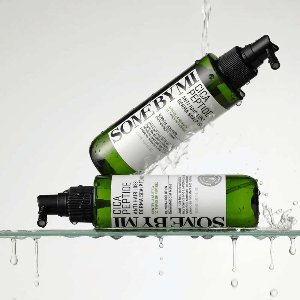 Due bottiglie SOME BY MI Cica Peptide Anti Hair Loss Derma Scalp Tonic giacciono dentro e sopra l'acqua con gocce che schizzano, bottiglie verdi con ugello spray nero ed etichetta bianca.