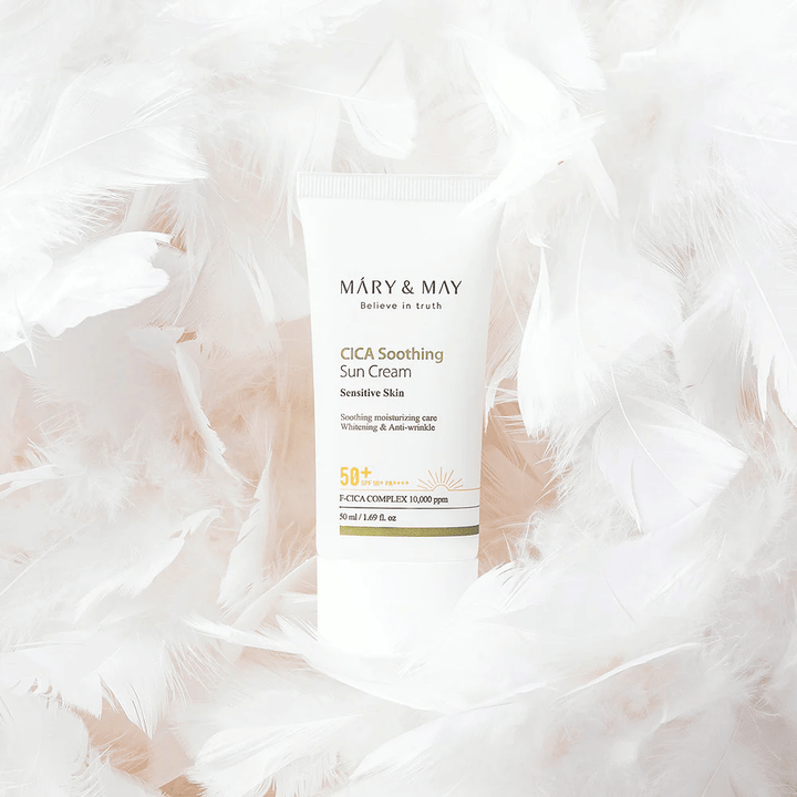 Mary&May CICA Soothing Sun Cream circondato da morbide piume bianche. L'immagine trasmette una sensazione di delicatezza, comfort e formula leggera adatta alla pelle sensibile.