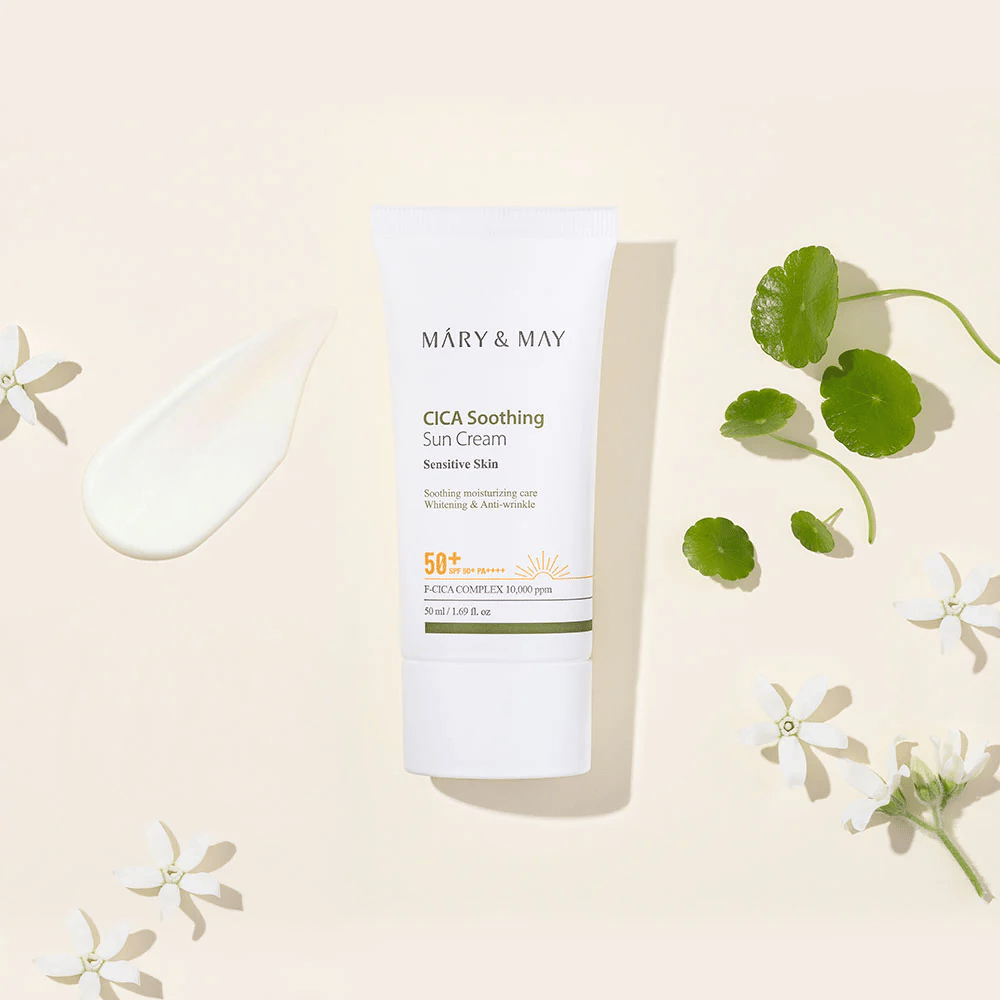 Mary&May CICA Soothing Sun Cream SPF50+ PA++++ presentata insieme a una texture cremosa, foglie di centella e fiori bianchi. L'immagine mette in risalto le proprietà lenitive del prodotto e l'attenzione alla pelle sensibile.