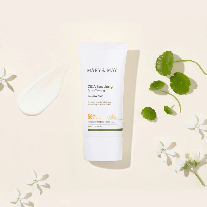 Mary&May CICA Soothing Sun Cream SPF50+ PA++++ presentata insieme a una texture cremosa, foglie di centella e fiori bianchi. L'immagine mette in risalto le proprietà lenitive del prodotto e l'attenzione alla pelle sensibile.