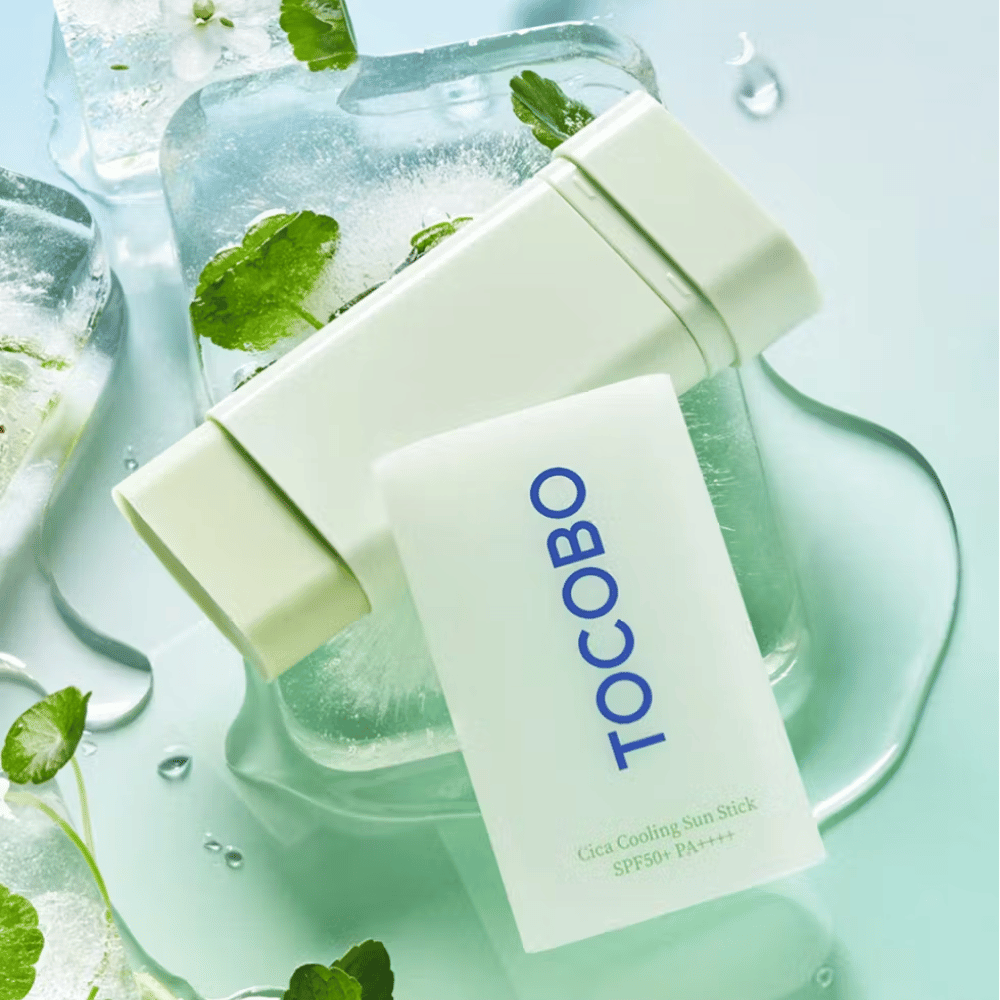 Tocobo Cica Cooling Sun Stick SPF50+ PA++++ su cubetti di ghiaccio con foglie di piante verdi, che trasmette una sensazione rinfrescante e refrigerante.
