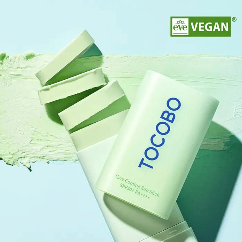 Tocobo Cica Cooling Sun Stick SPF50+ PA++++ in confezione verde chiaro con marchio vegano (EVE VEGAN), posizionata su uno strato di stick solare verde.