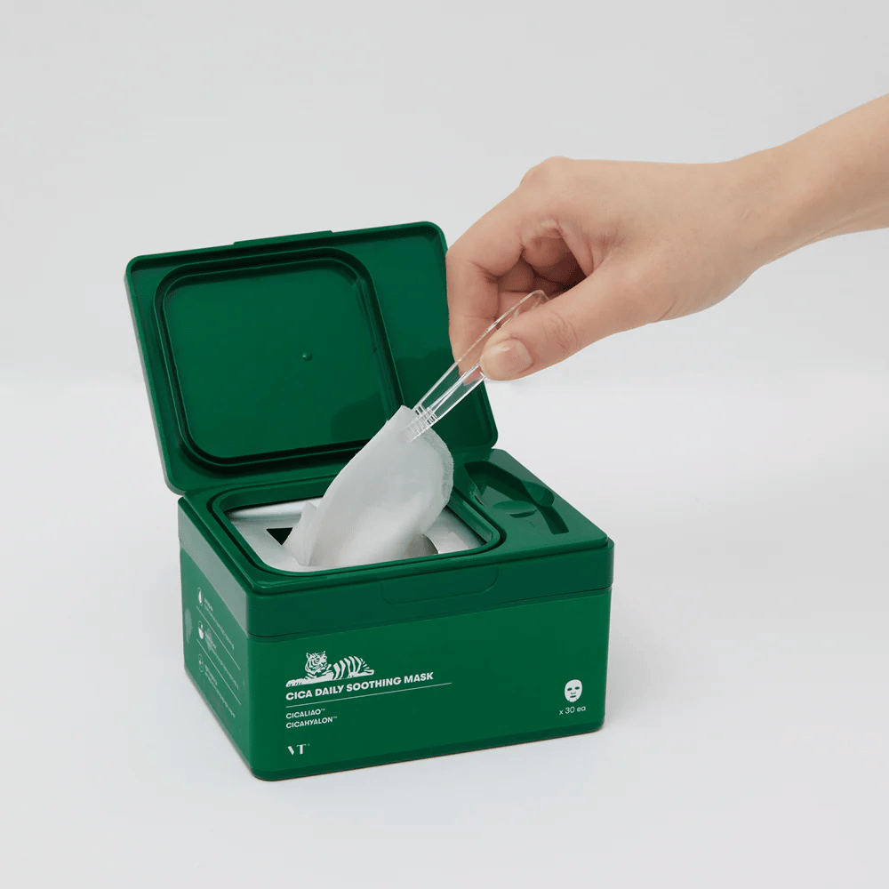Mano utilizza una pinzetta per prendere un sheet mask da un contenitore verde etichettato "Cica Daily Soothing Mask".