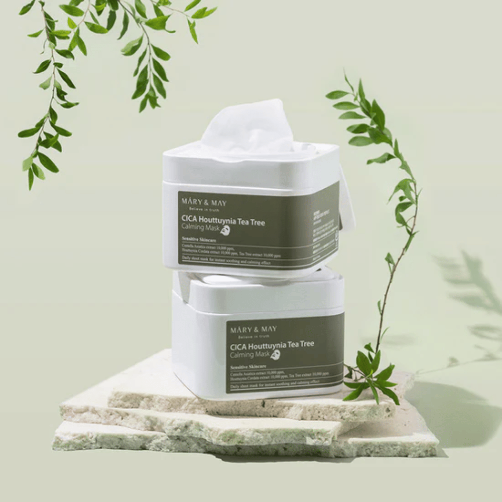 Due barattoli di Mary & May Cica Houttuynia Tea Tree Calming Mask posizionati su pietra naturale con dettagli di piante verdi – maschere in tessuto lenitive per pelle sensibile.