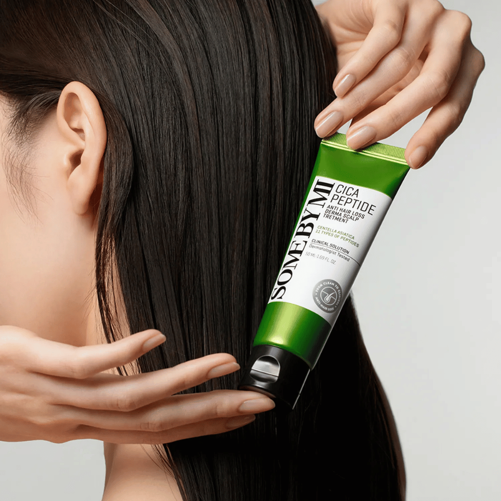 Donna applica SOME BY MI Cica Peptide Anti Hair Loss Derma Scalp Treatment in capelli lunghi e scuri con un tubo verde e bianco.