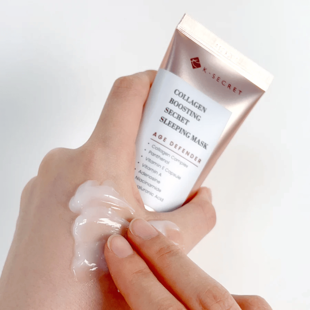 Una mano tiene Collagen Boosting Secret Sleeping Mask mentre l'altra applica una generosa quantità di crema sul dorso della mano – mostra la consistenza e l'applicazione del prodotto.