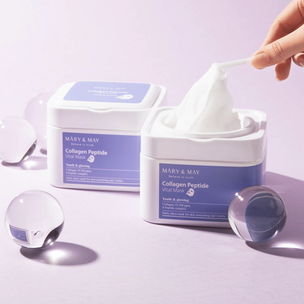 Una mano prende una maschera da un barattolo di MARY & MAY Collagen Peptide Vital Mask. La maschera è destinata all'uso quotidiano per nutrire e illuminare la pelle, con collagene e peptidi per sostenere la giovinezza della pelle.