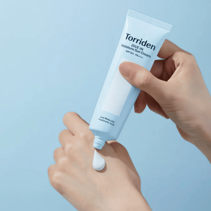 Torriden DIVE-IN Moisture Sun Cream SPF50+ PA++++ applicato sulla mano per mostrare la consistenza leggera e cremosa della crema solare idratante.