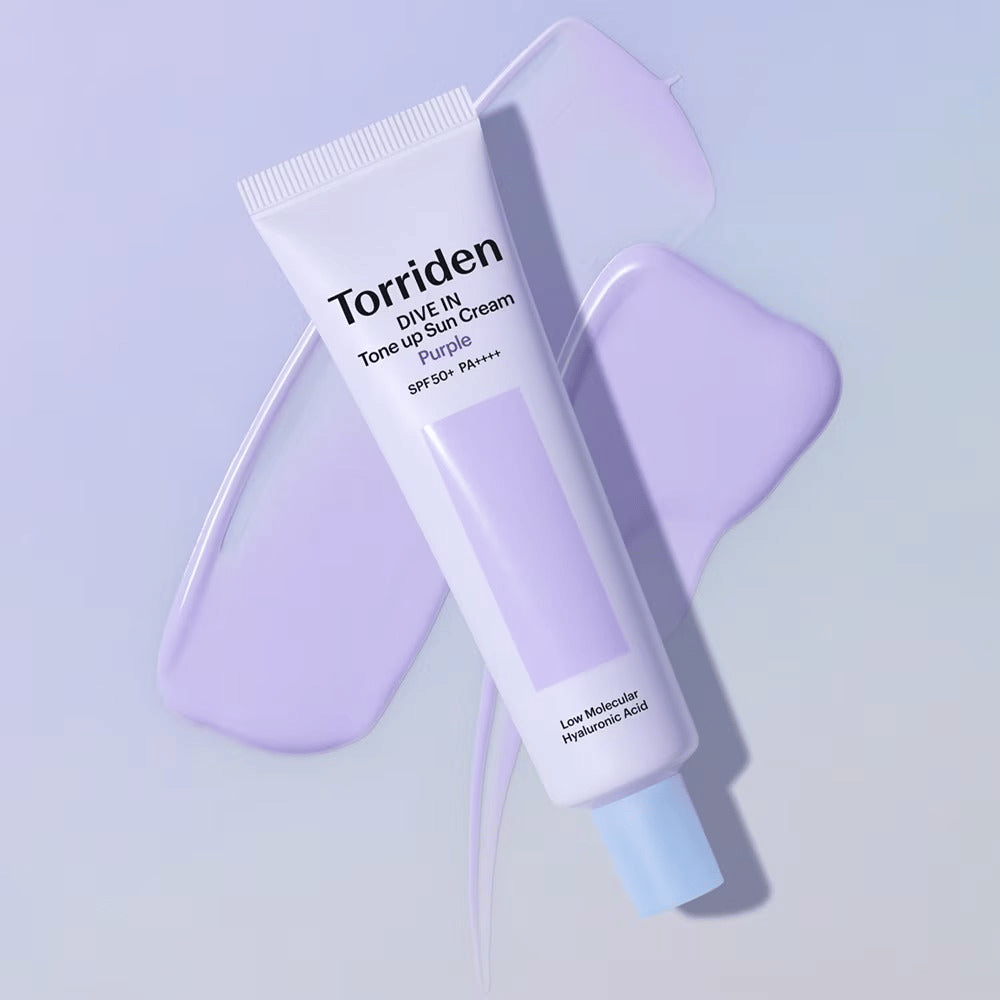 Torriden DIVE IN Tone Up Sun Cream Purple posizionato su crema viola spalmata che evidenzia l'effetto uniformante e illuminante.