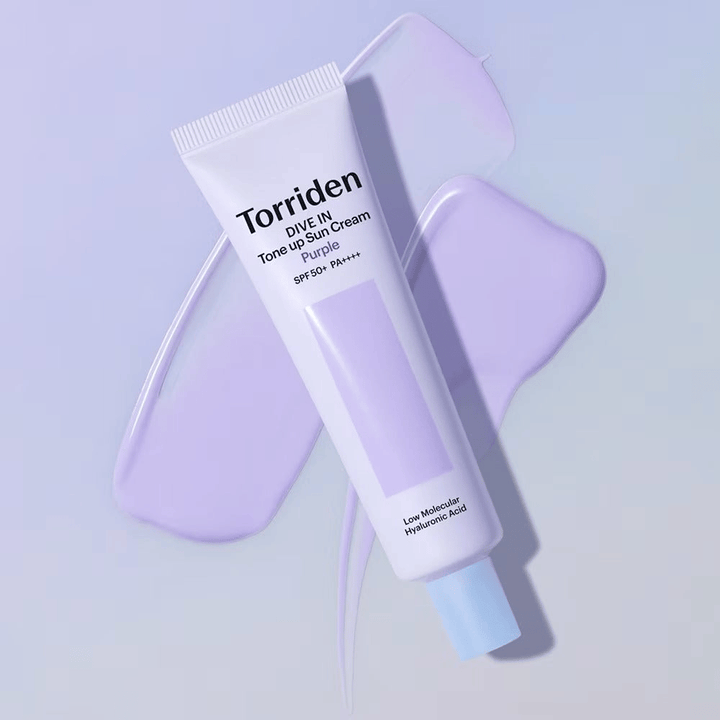 Torriden DIVE IN Tone Up Sun Cream Purple posizionato su crema viola spalmata che evidenzia l'effetto uniformante e illuminante.