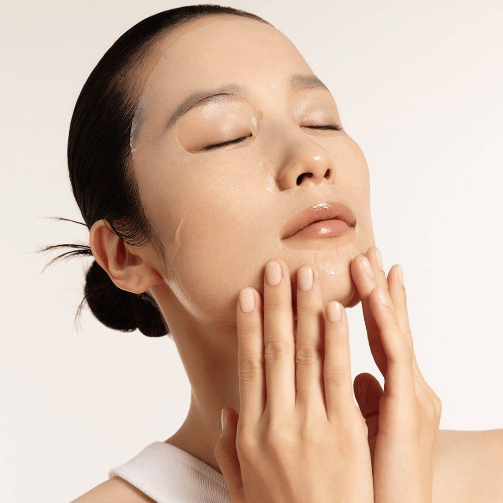 Modello con pelle idratata e luminosa che applica sheet mask, focus su luminosità, tono uniforme della pelle e glow.