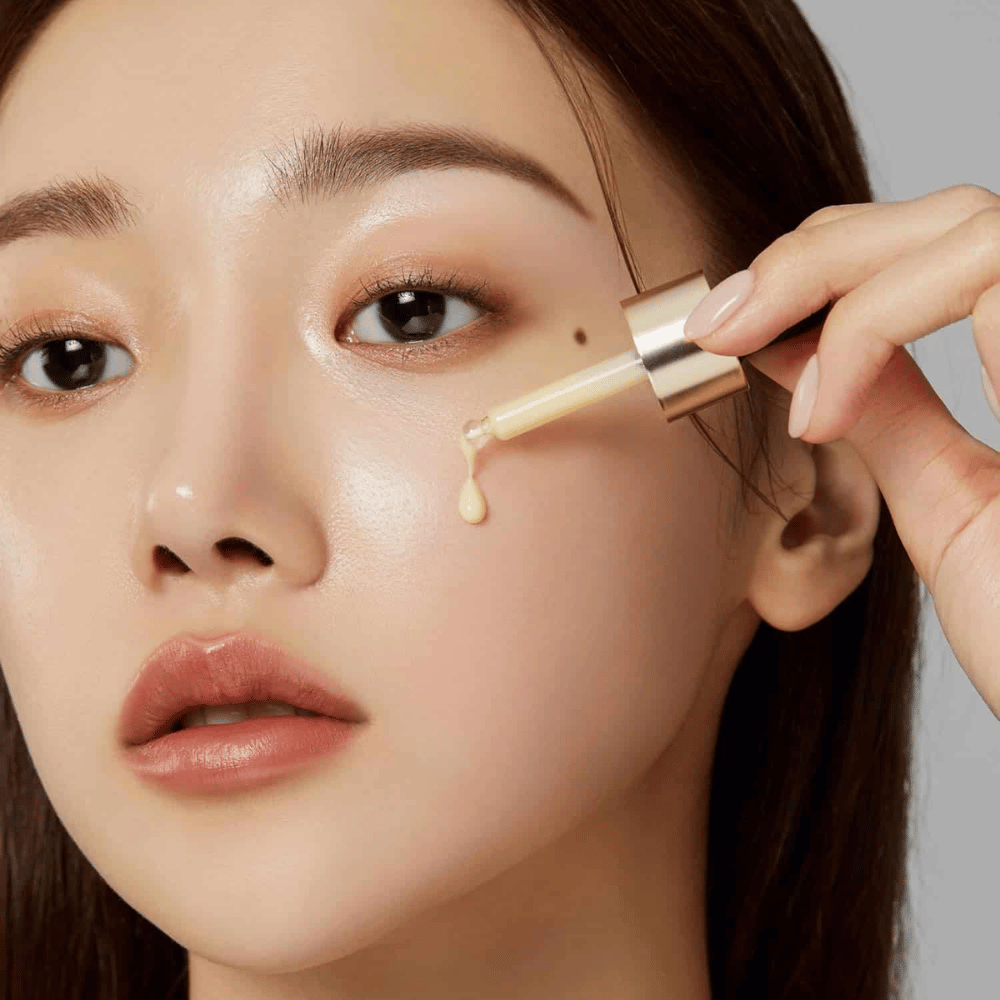 Primo piano di una donna che applica Medicube Deep Vita C Ampoule con una pipetta dorata. Una goccia del siero sta per raggiungere la sua pelle, che ha una luminosità naturale. Perfetto per dare un tono della pelle più luminoso e uniforme.